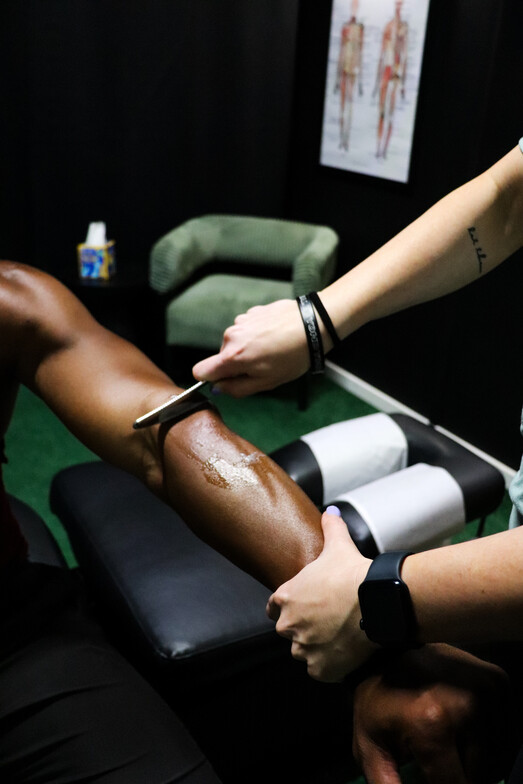 Dr. Taylor Hartman using a stainless steel IASTM tool to perform soft tissue scraping on a patient’s elbow to treat an overuse injury.
