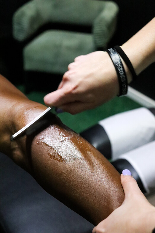 Chiropractor using Graston Technique instrument-assisted soft tissue therapy on a patient's outer thigh to treat IT band syndrome at Limitless Sports Chiropractic in Oak Point, TX