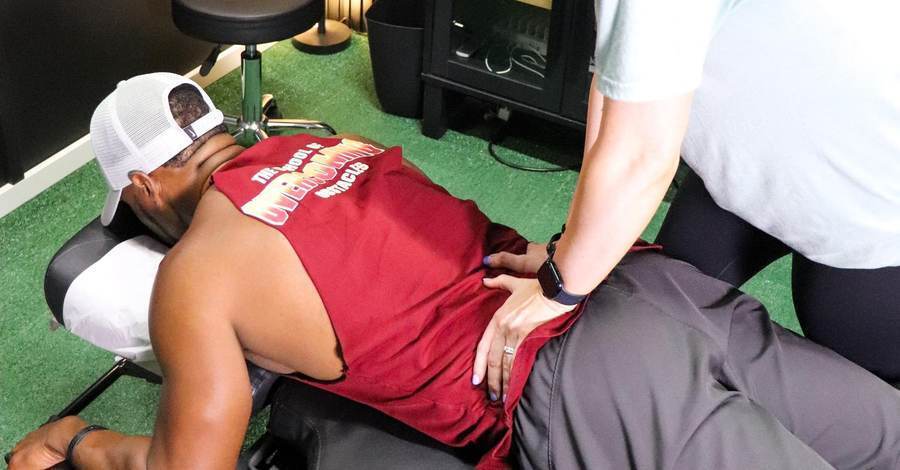 Chiropractor performing a prone thoracic spine adjustment on a male athlete lying face down on a treatment table, with a spine anatomy chart visible in the background at Limitless Sports Chiropractic.