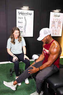 Clinician performing a hip and knee flexion mobility assessment on a male patient seated on a treatment table, the type of evaluation used before Active Release Technique treatment for piriformis syndrome at Limitless Sports Chiropractic.