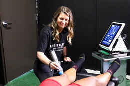 Shockwave therapy device being applied to a patient's lower leg, the same treatment approach used to treat prepatellar knee bursitis at Limitless Sports Chiropractic.