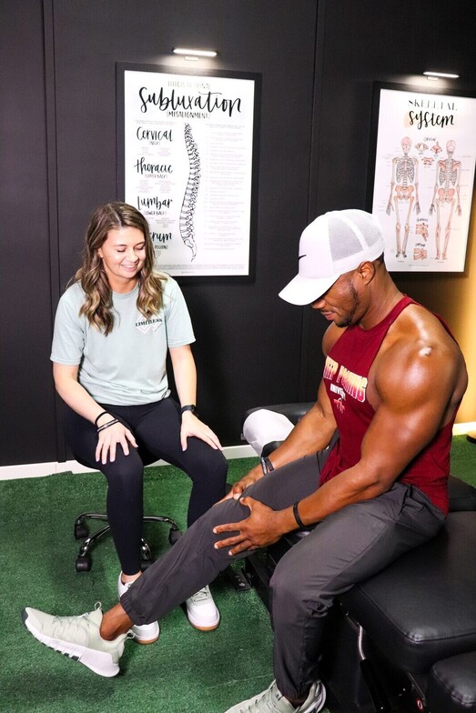 Clinician performing a hip and knee flexion mobility assessment on a male patient seated on a treatment table, the type of evaluation used before myofascial release treatment for piriformis syndrome at Limitless Sports Chiropractic.